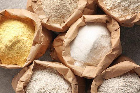 A top view of multiple different types of flours in brown paper bags
