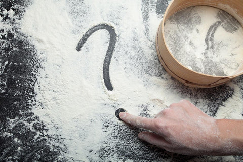 Flour dusted on a black table with a hand drawing a question mark in the flour